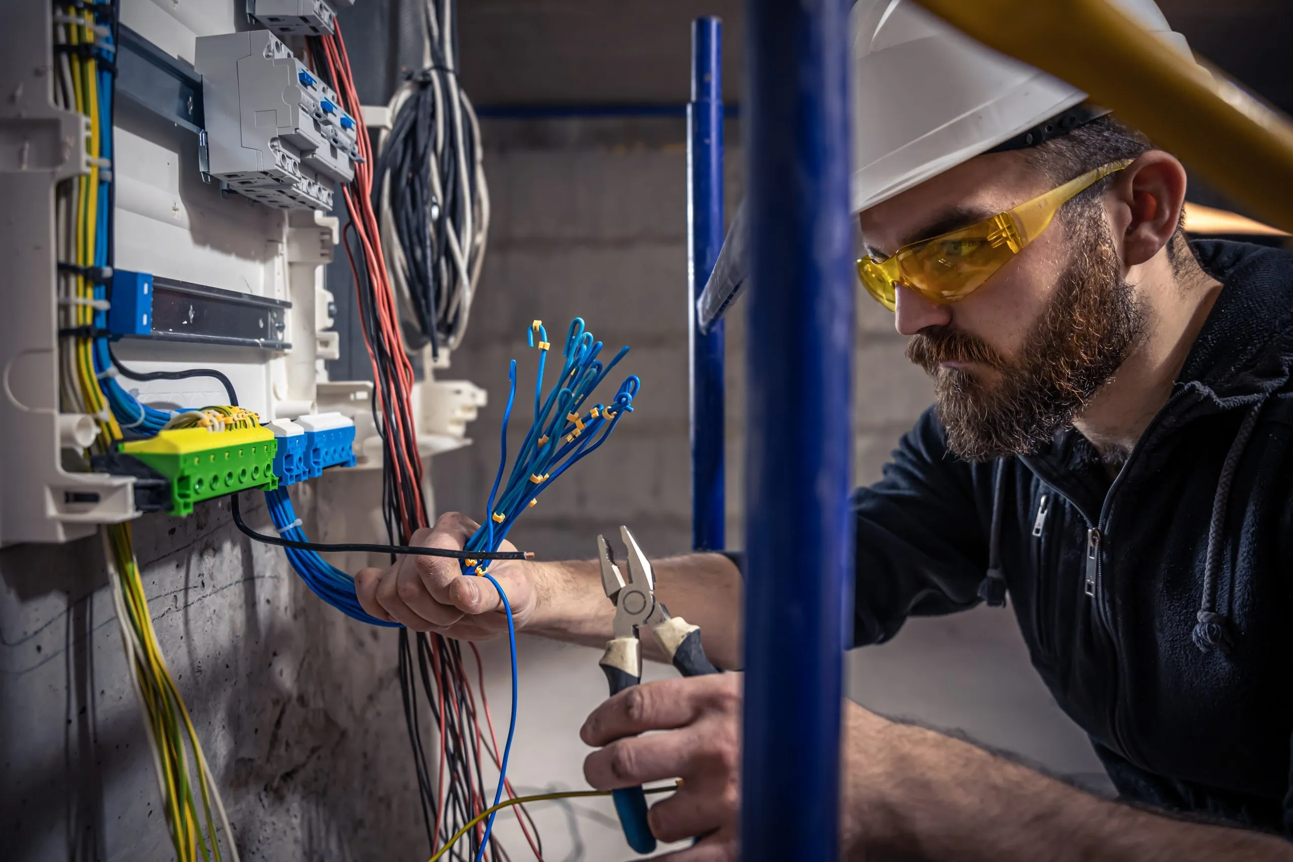 A male electrician works in a switchboard with an electrical connecting cable, connects the equipment with tools.